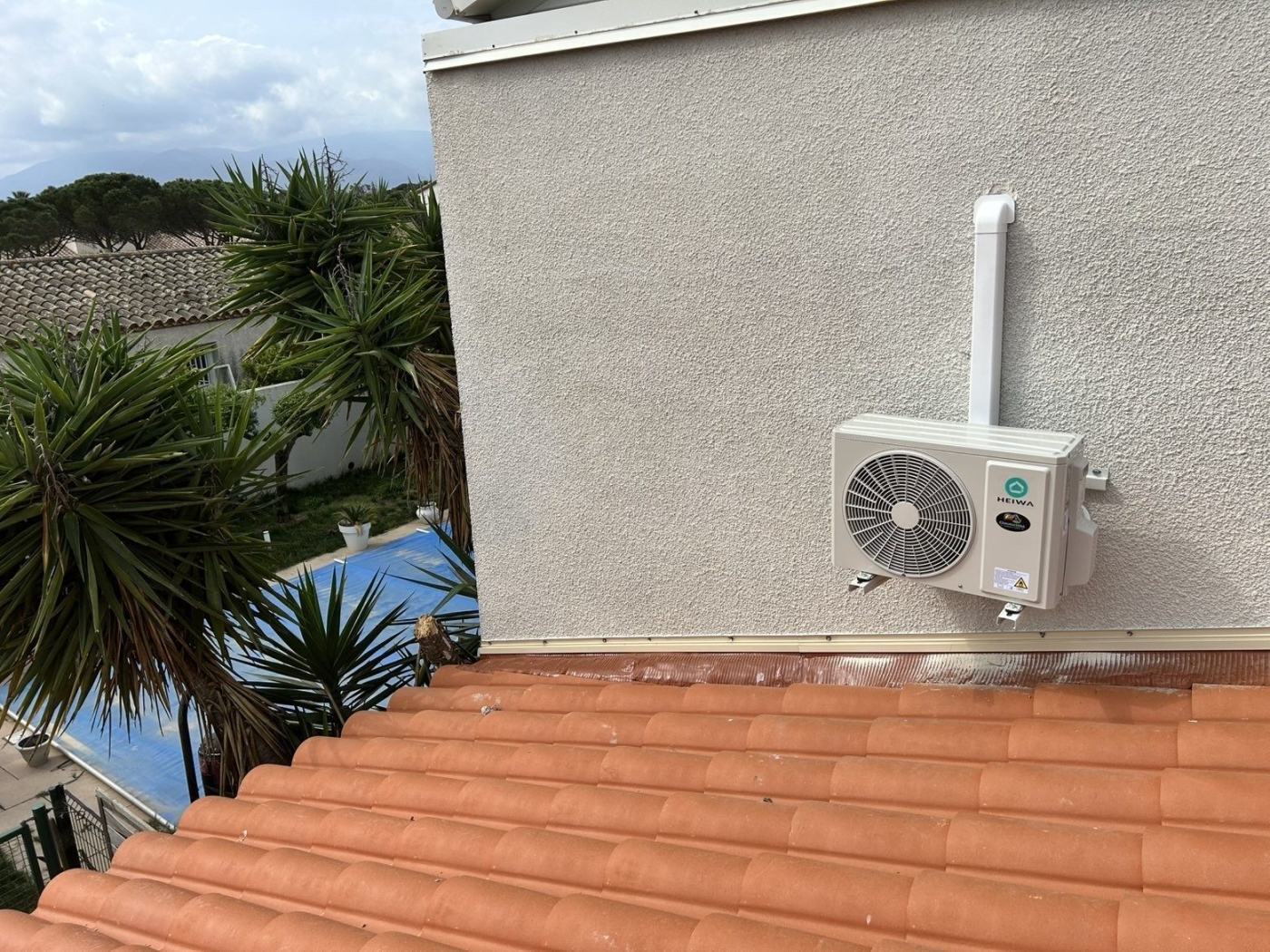 Groupe extérieur de climatisation fixé en façade au-dessus d'une toiture en tuiles